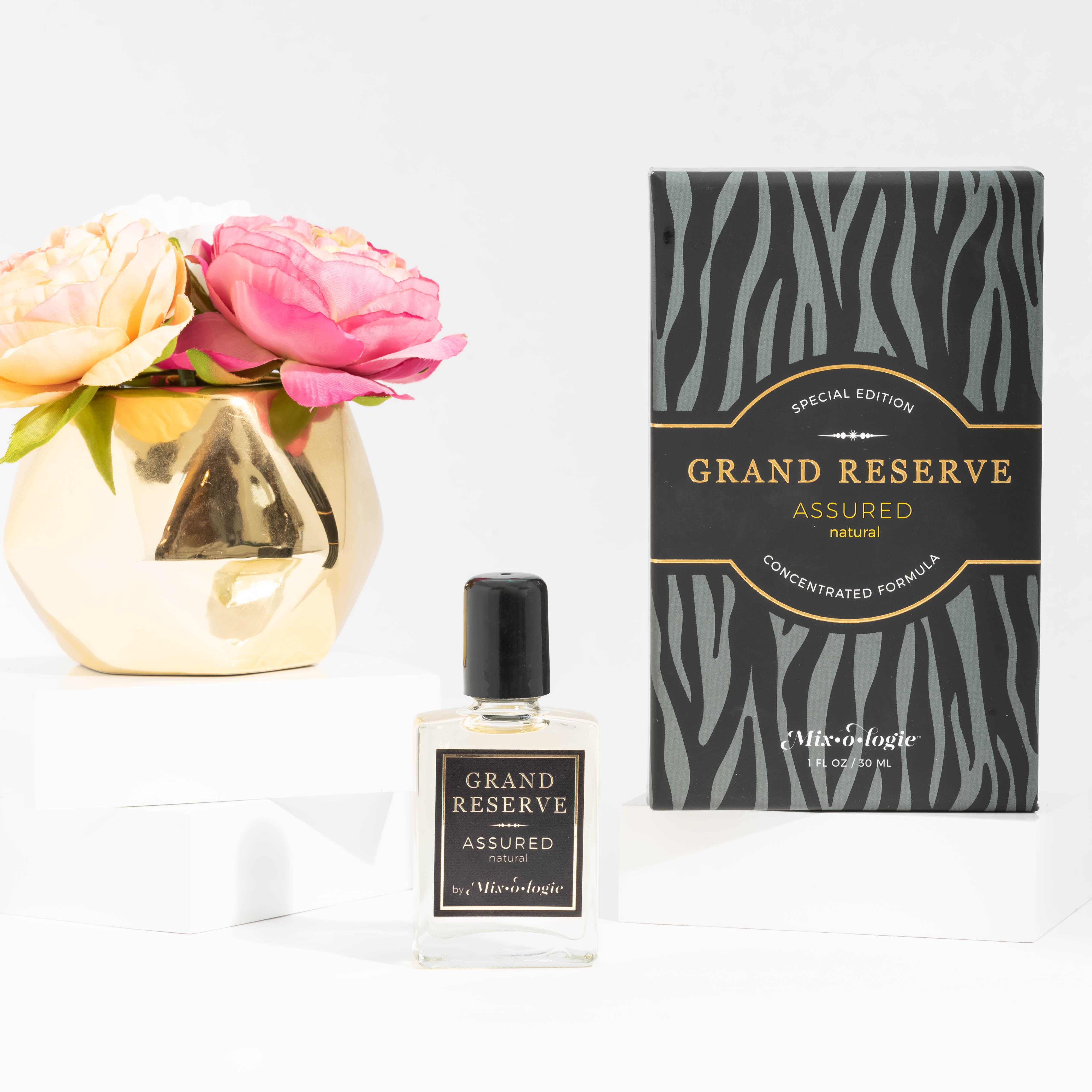 Assured (Natural) Special Edition Grand Reserve concentrated formula in clear glass rectangle perfume bottle that has 1 fl oz or 30 mL of light-yellow liquid with black cap, label, and spray nozzle. Black zebra pattern rectangle box with mustard letting. Grand Reserve and box pictured with white background and gold vase with pink flowers.