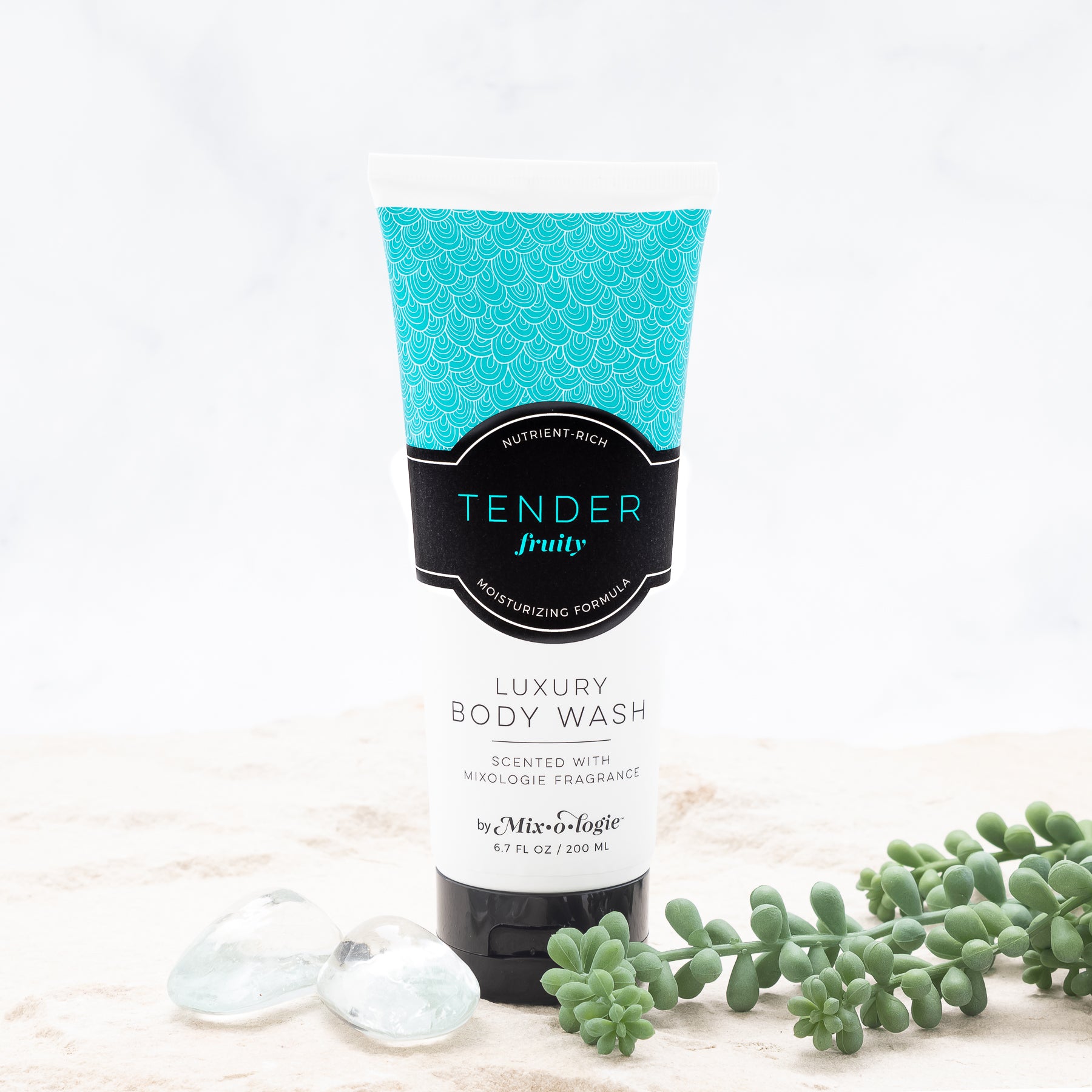 Luxury Body Wash in Mixologie’s Tender (Fruity) in bright blue color sample package with black label. Contains 6.7 fl oz or 200 mL pictured in sand with rocks and greenery.