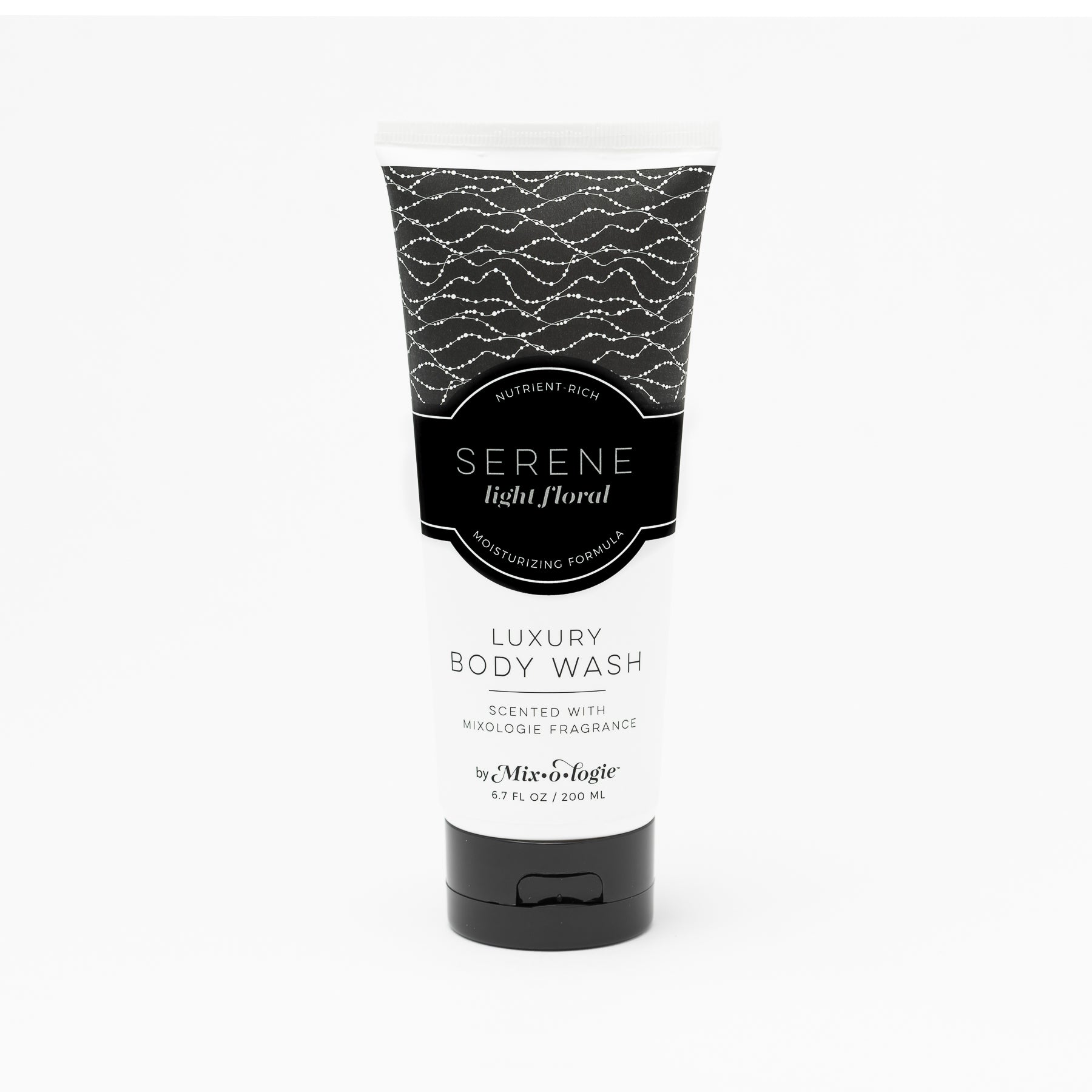 Luxury Body Wash in Serene (Light Floral) in white pattern package and black label in the sand with rocks and greenery .Contains 6.7 fl oz or 200 mL.