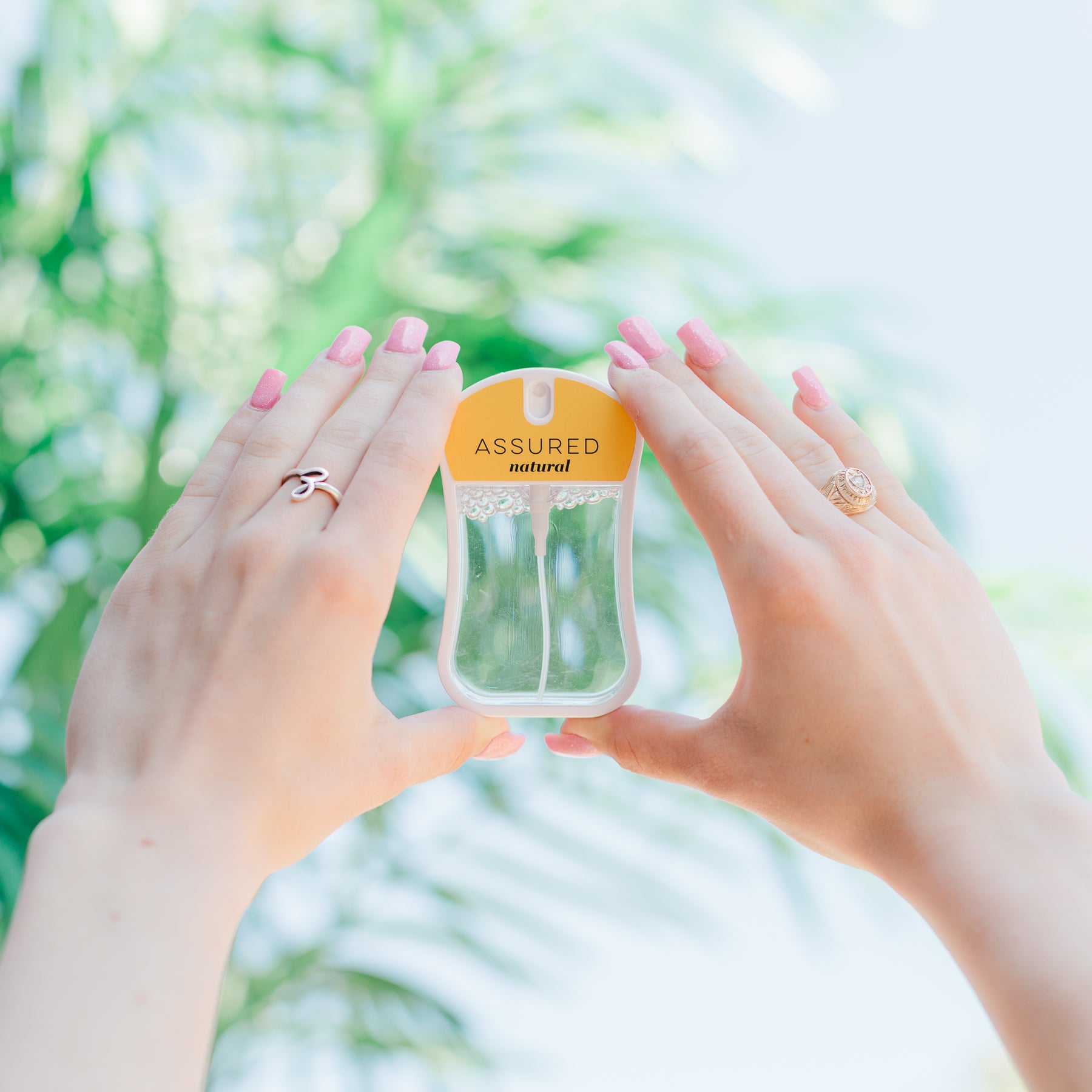 Assured (Natura) Moisturizing Body Mist in mustard color box and spray bottle with mustard color label and clear liquid. Spray bottle has 1.1 fl oz or 35 mL. Spray bottle is held in models hands with trees in background