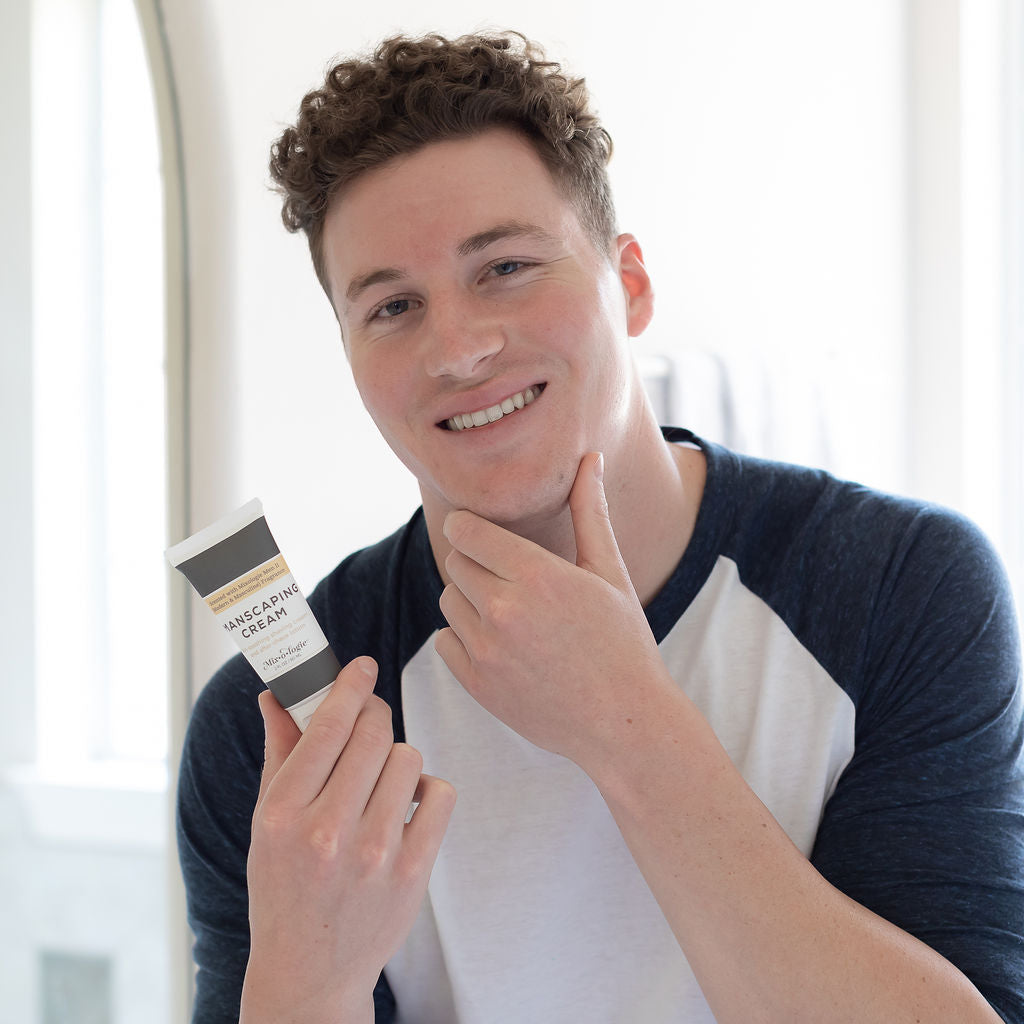 Men’s Manscaping Cream in Men’s II (Modern & Masculine) in a black and white tube with yellow accents. Skin-soothing shaving cream and after-shave lotion. 2 fl oz or 60 mL. Pictured in model's hands