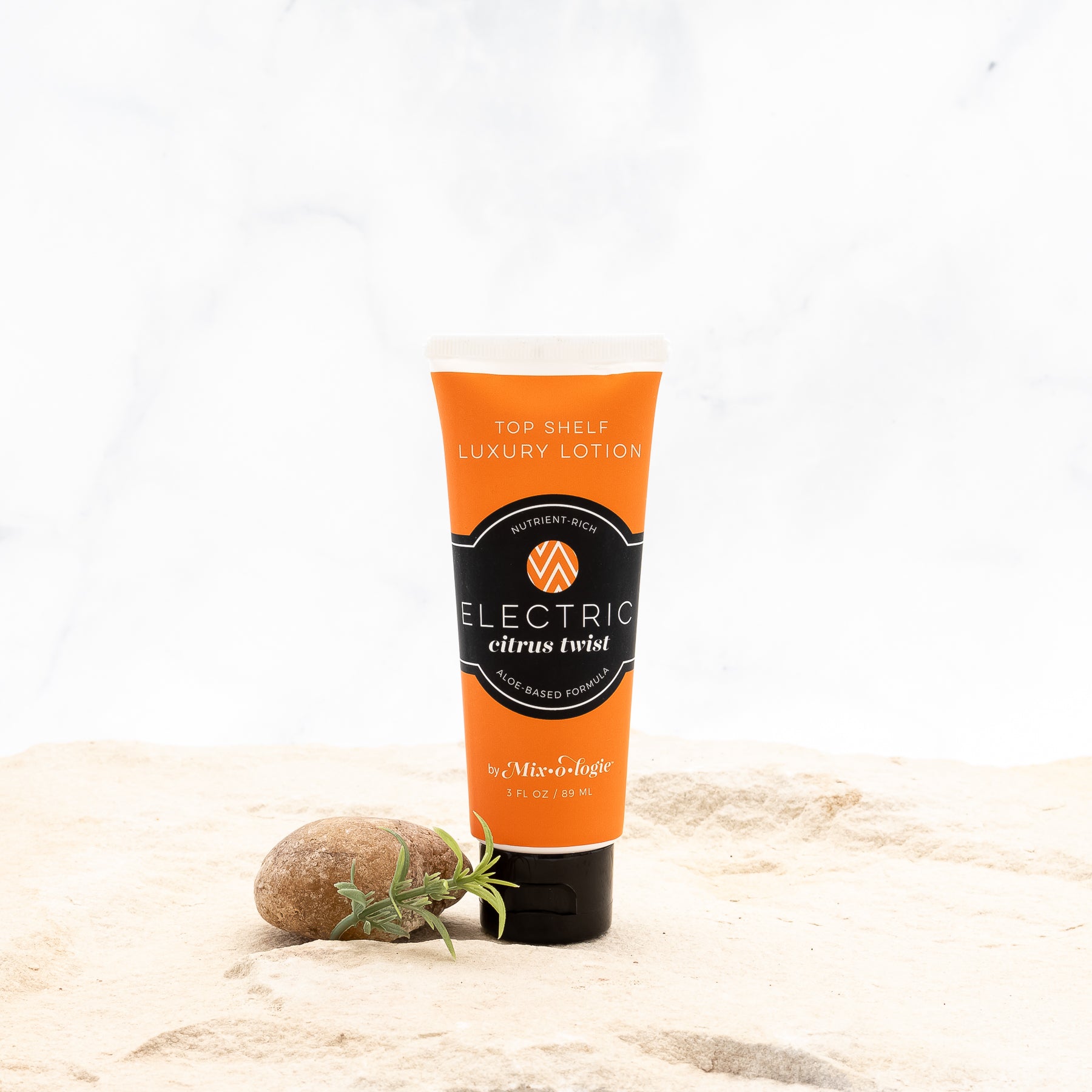 Electric (Citrus Twist) Top Shelf Lotion in orange tube with black lid and label. Nutrient rich, aloe-based formula, tube has 5 fl oz or 89 mL. Pictured with white background, sand, rocks, and greenery. 