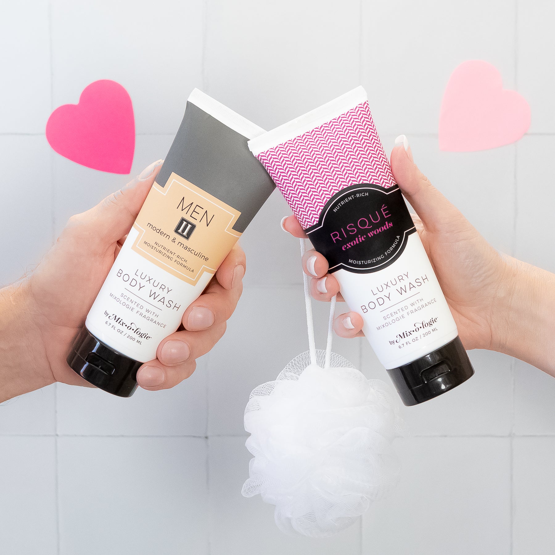 2 Body Wash tubes being held by hands in shower with hearts.  Scents of the body wash are Men's II and Risque (exotic woods)