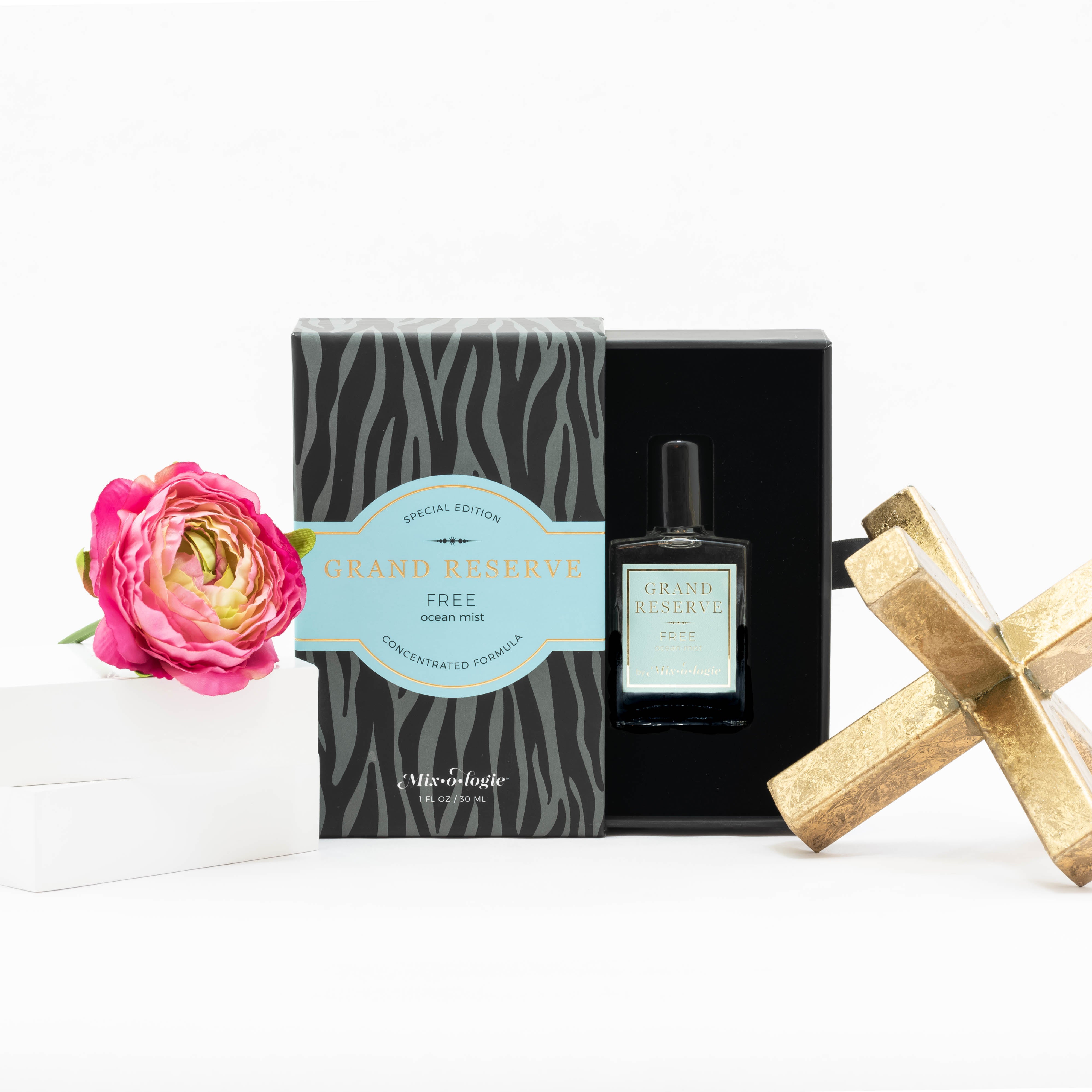 Free (Ocean Mist) Special Edition Grand Reserve concentrated formula in clear glass rectangle perfume bottle that has 1 fl oz or 30 mL of clear liquid with black cap, label, and spray nozzle. Black zebra pattern rectangle box with pale blue letting. Grand Reserve and box pictured with white background pink flower and gold table décor.