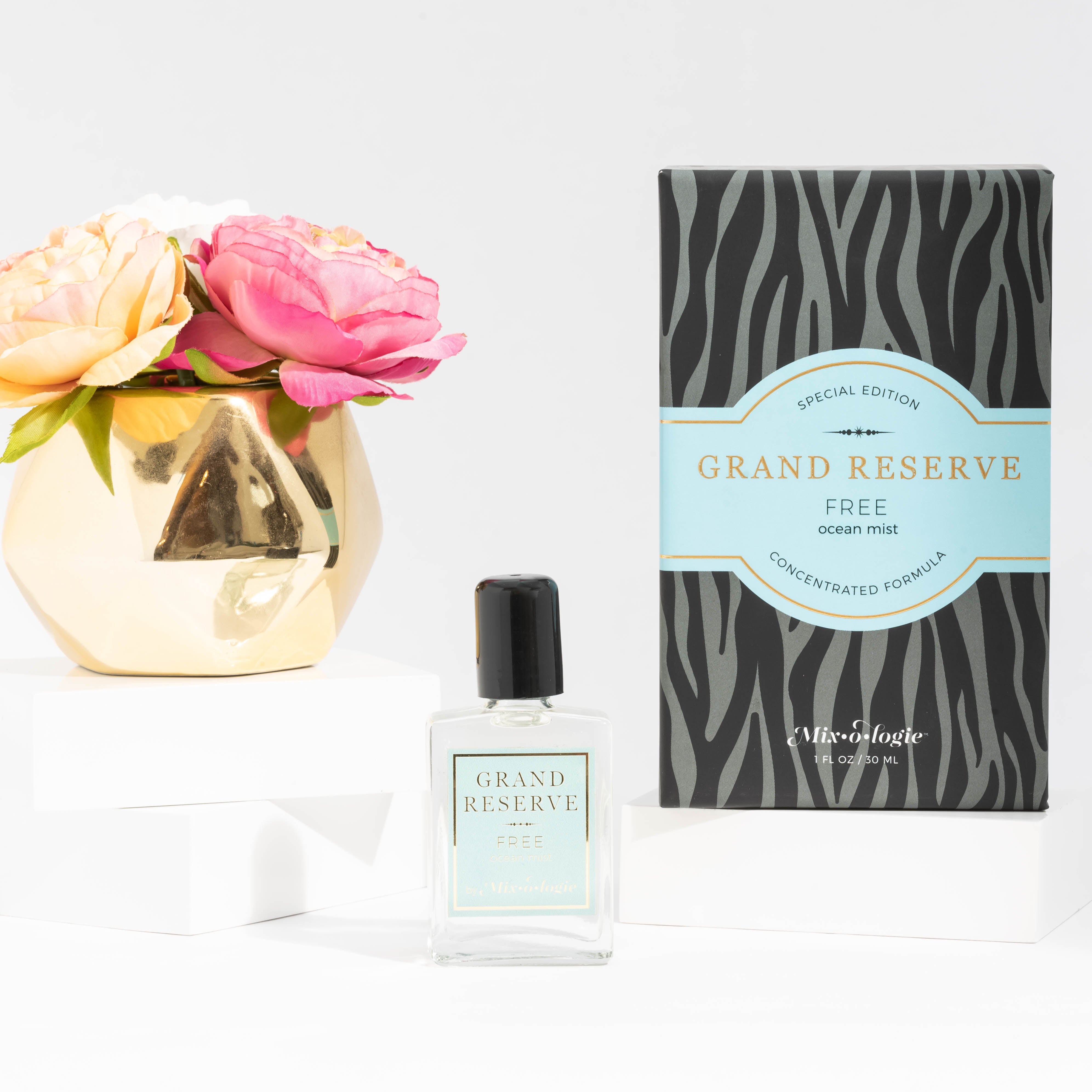 Free (Ocean Mist) Special Edition Grand Reserve concentrated formula in clear glass rectangle perfume bottle that has 1 fl oz or 30 mL of clear liquid with black cap, label, and spray nozzle. Black zebra pattern rectangle box with pale blue letting. Grand Reserve and box pictured with white background pink flower and gold table décor.