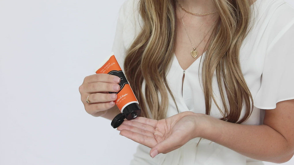 Electric (Citrus Twist) Top Shelf Lotion in orange tube with black lid and label. Nutrient rich, aloe-based formula, tube has 5 fl oz or 89 mL. Pictured with model applying to hands and smelling the scent then smiling.  