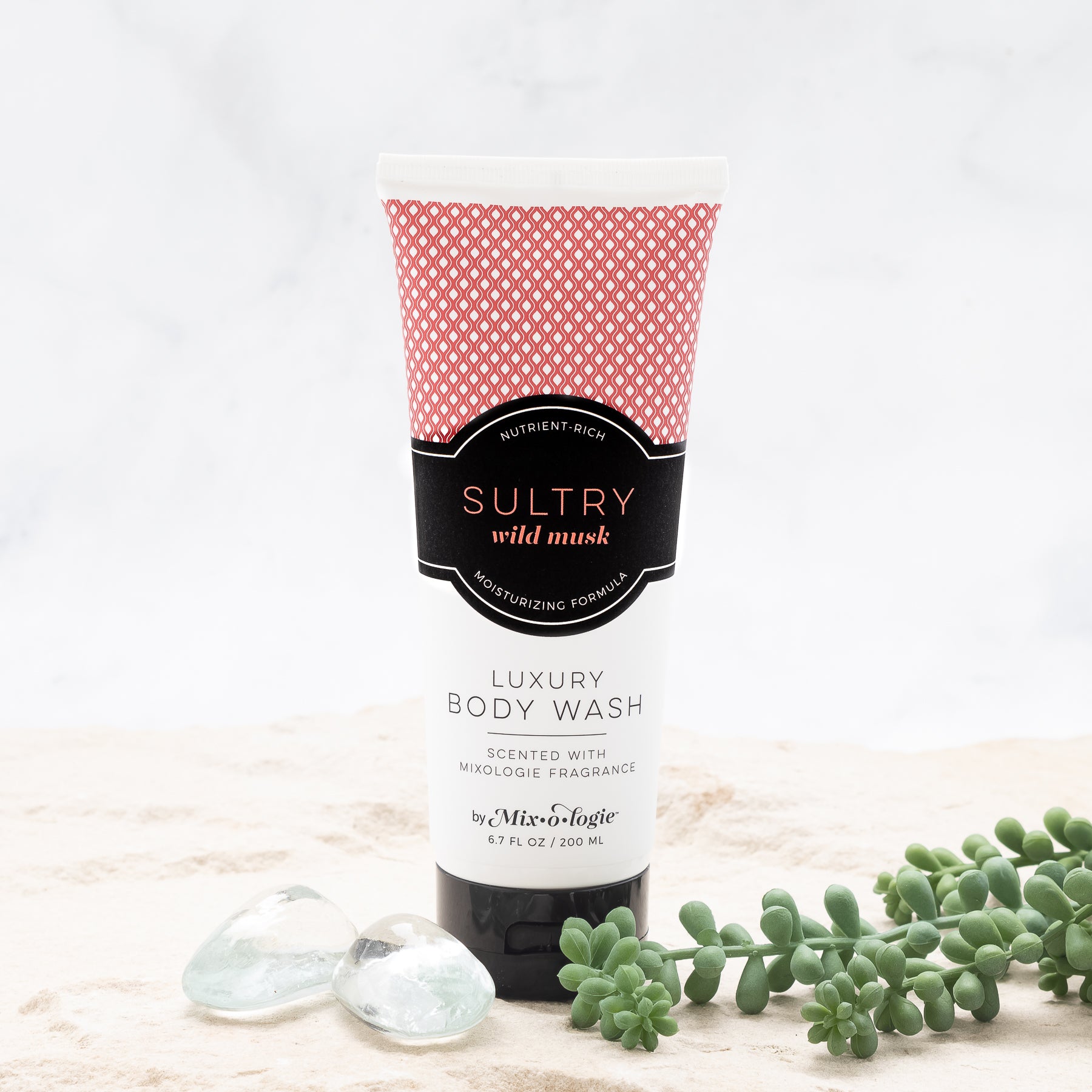Luxury Body Wash in Mixologie’s Sultry (Wild Musk) in red color sample package with black label. Contains 6.7 fl oz or 200 mL pictured in sand with rocks and greenery.