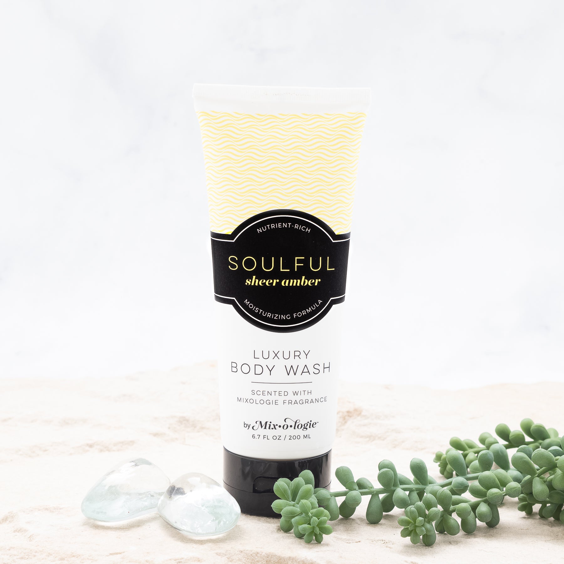 Luxury Body Wash in Mixologie’s Soulful (Sheer Amber) in bright yellow color sample package with black label. Contains 6.7 fl oz or 200 mL pictured on a white background with sand, rocks, and greenery.