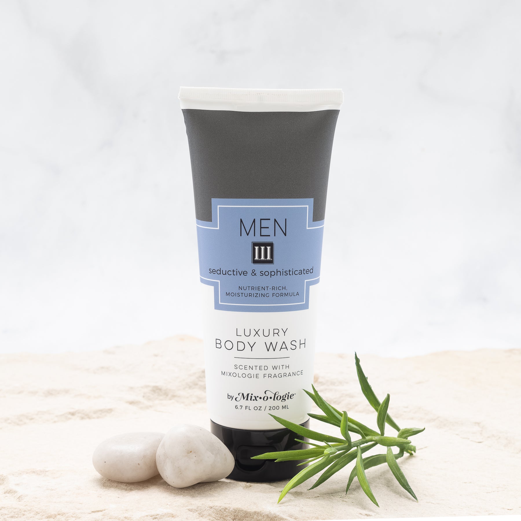 Luxury Body Wash in Men III (Seductive & Sophisticated) in grey color package with blue label in sand with rocks and greenery.