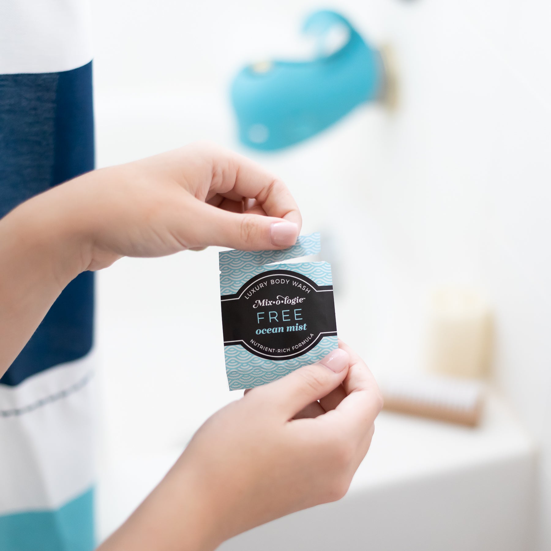 Luxury Body Wash Sample of Free (Ocean Mist) in light blue pattern with black label being modeled into hand with bathtub in background