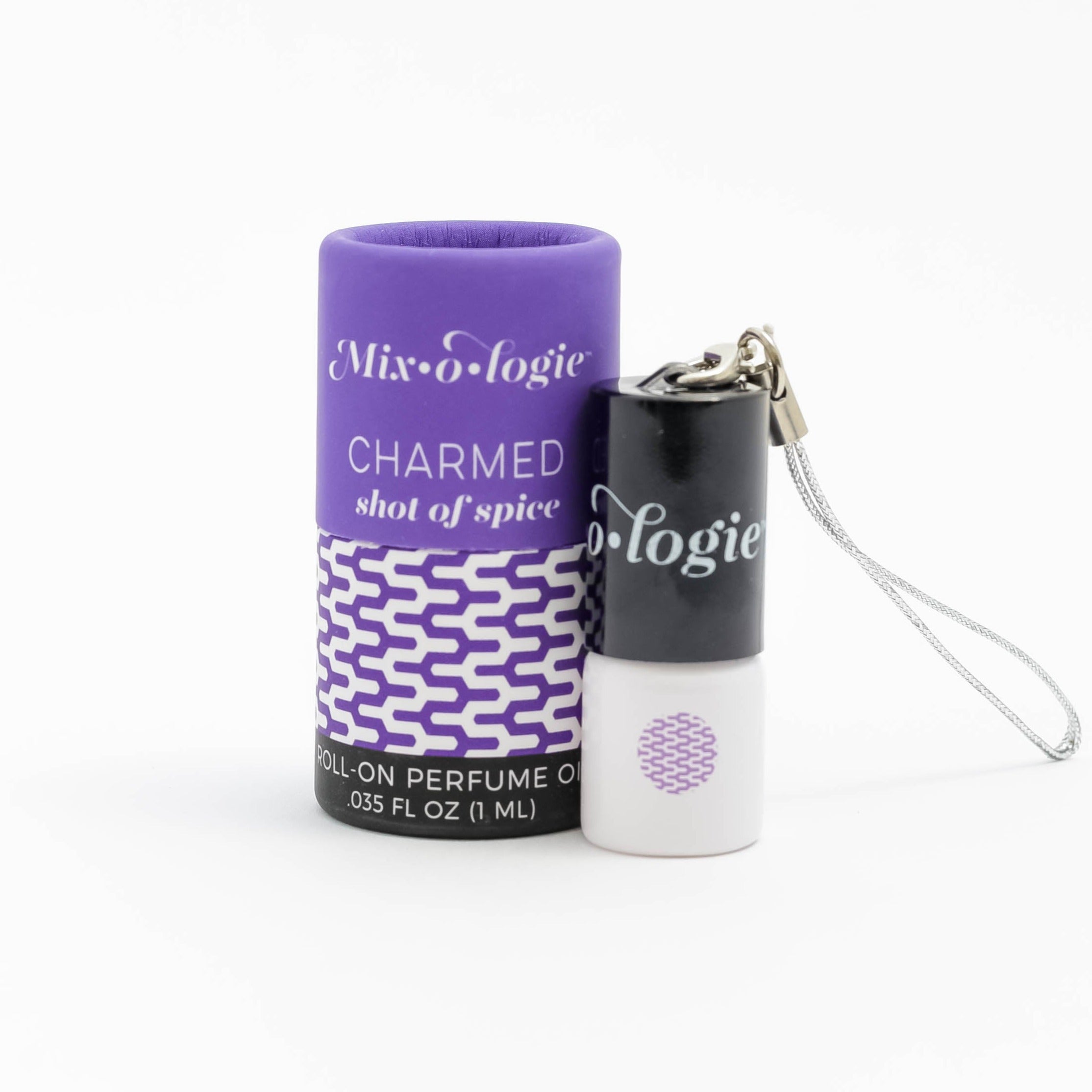 Charmed (Shot of Spice) mini white cylinder rollerballs with black top and keychain attachment with dark purple pattern has .035 fl oz or 1 mL. Dark purple cylinder packing tube with dark purple pattern. Roll-on perfume oil. Mini rollerball and cylinder tube are on a white background