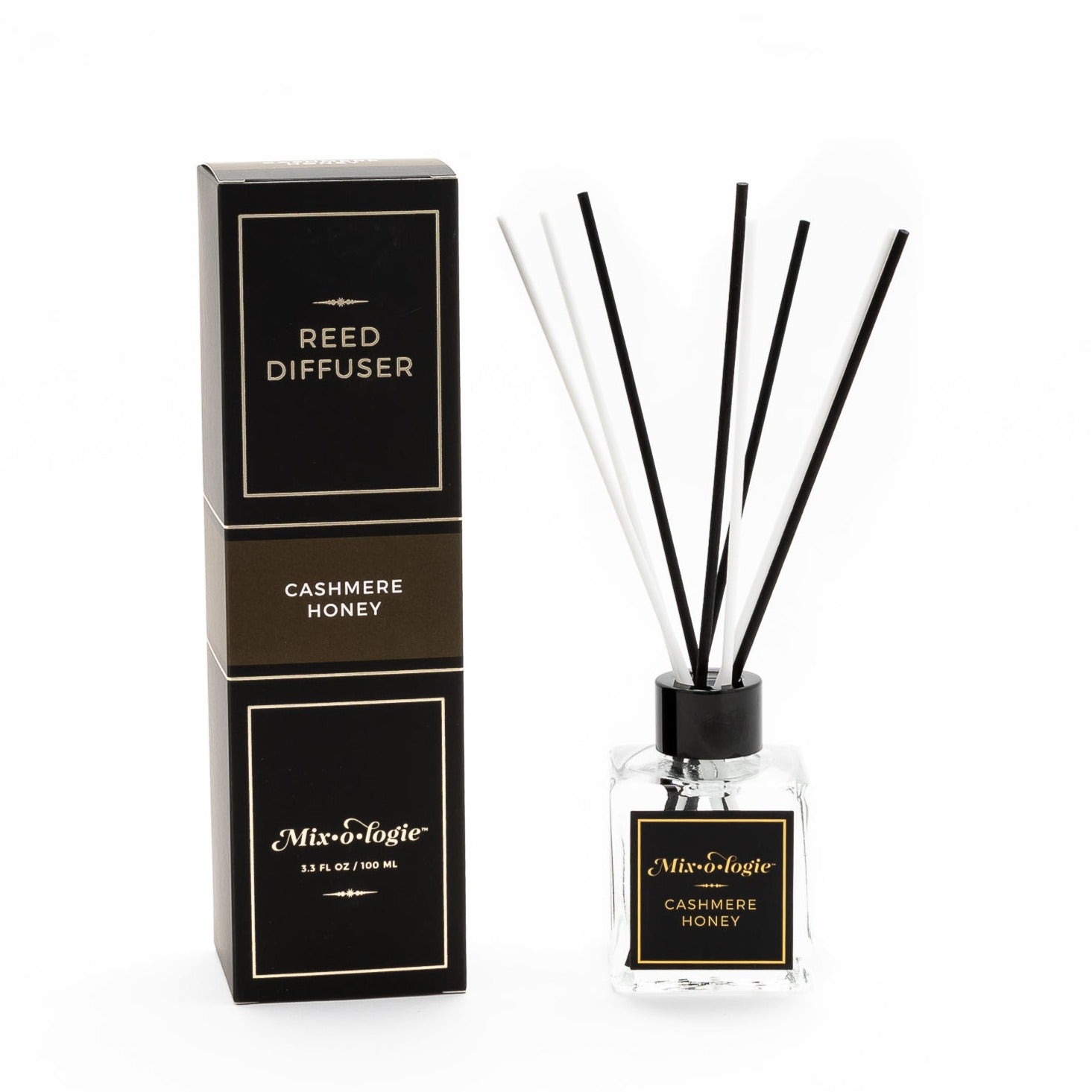 Cashmere Honey Reed Diffuser is a clear square glass container with black label that says Mixologie – Cashmere Honey. Has a black top and 4 white & 4 black reed sticks coming out of top, is 3.3 fl oz or 100 mL of clear scented liquid. Black rectangle package box with brown label. Box and diffuser are pictured with white background