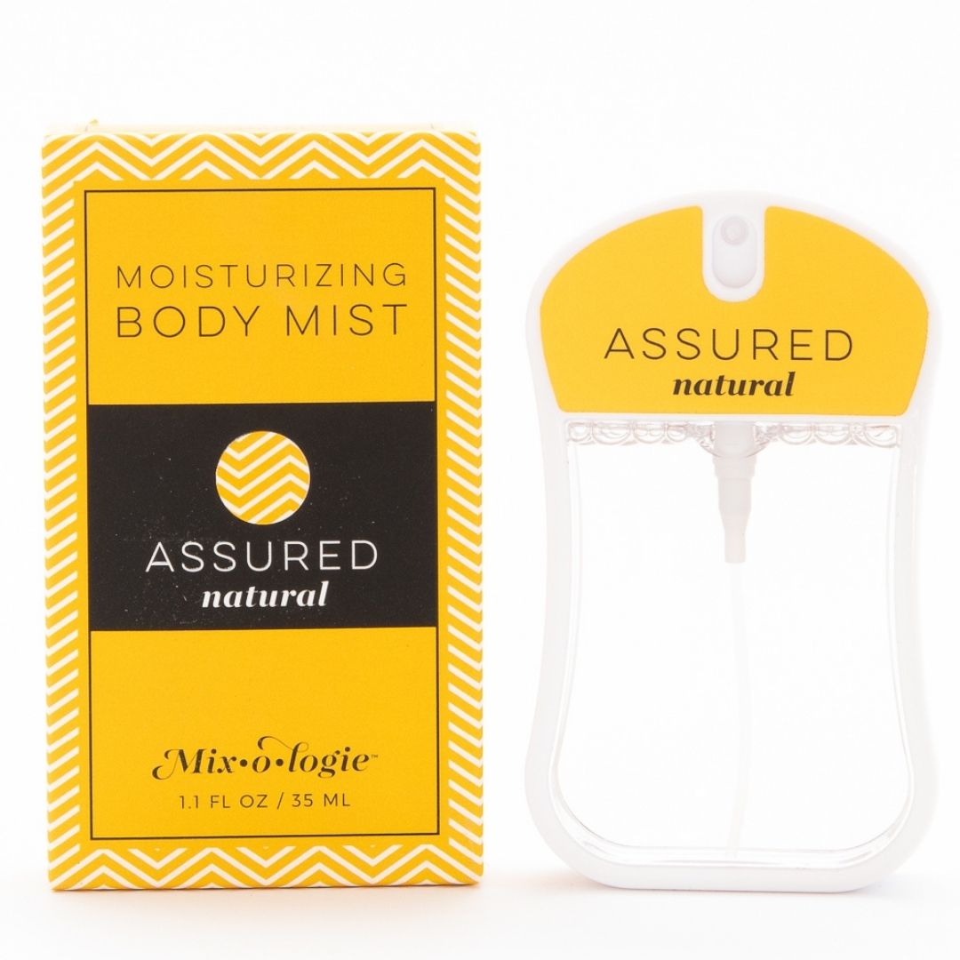 Assured (Natura) Moisturizing Body Mist in mustard color box and rounded rectangle spray bottle with mustard color label and clear liquid. Spray bottle has 1.1 fl oz or 35 mL. Spray bottle and box are pictured with a white background.  