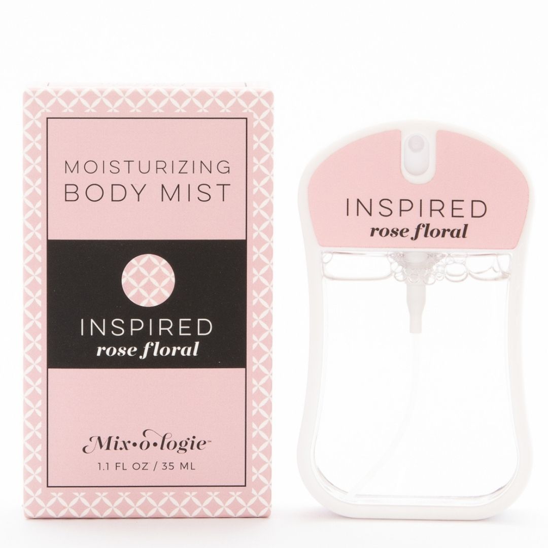 Inspired (Rose Floral) Moisturizing Body Mist in pale pink color box and rounded rectangle spray bottle with pale pink color label and clear liquid. Spray bottle has 1.1 fl oz or 35 ML. Spray bottle and box are pictured in the sand on white background.