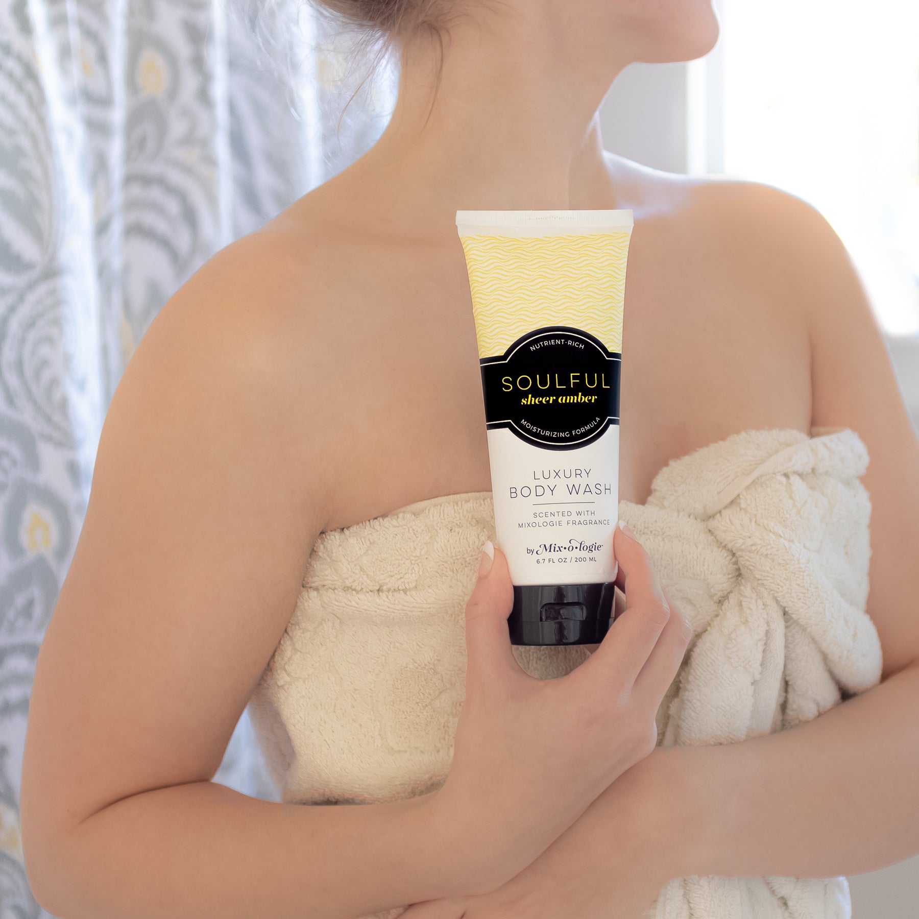 Luxury Body Wash in Mixologie’s Soulful (Sheer Amber) in bright yellow color sample package with black label. Contains 6.7 fl oz or 200 mL pictured in models hands in a bathroom.
